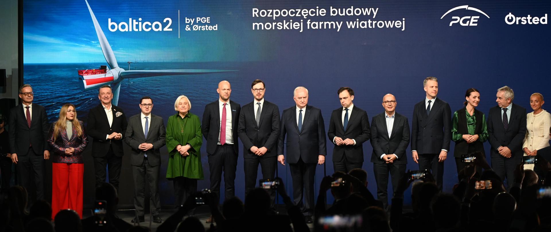 Minister Jakub Jaworowski i inni uczestnicy wydarzenia stoją na scenie. W tle ścianka z napisem: Rozpoczęcie budowy morskiej farmy wiatrowej oraz logotypy PGE i Orsted.