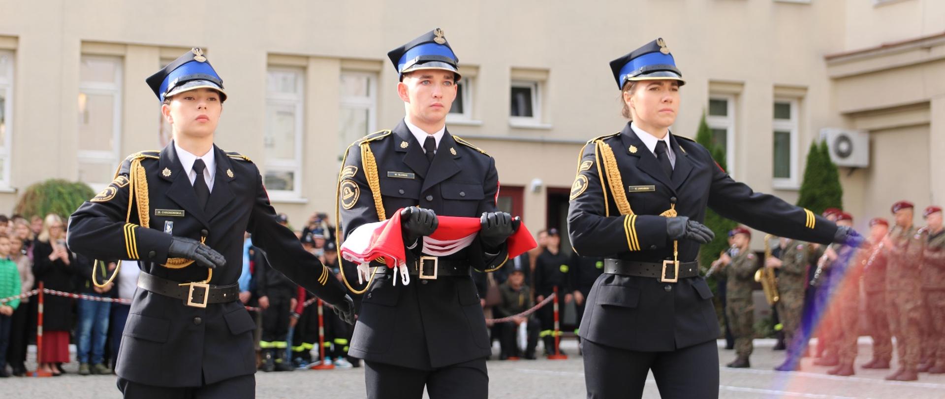 Poczet flagowy maszeruje w kierunku masztu do podniesienia flagi państowej.