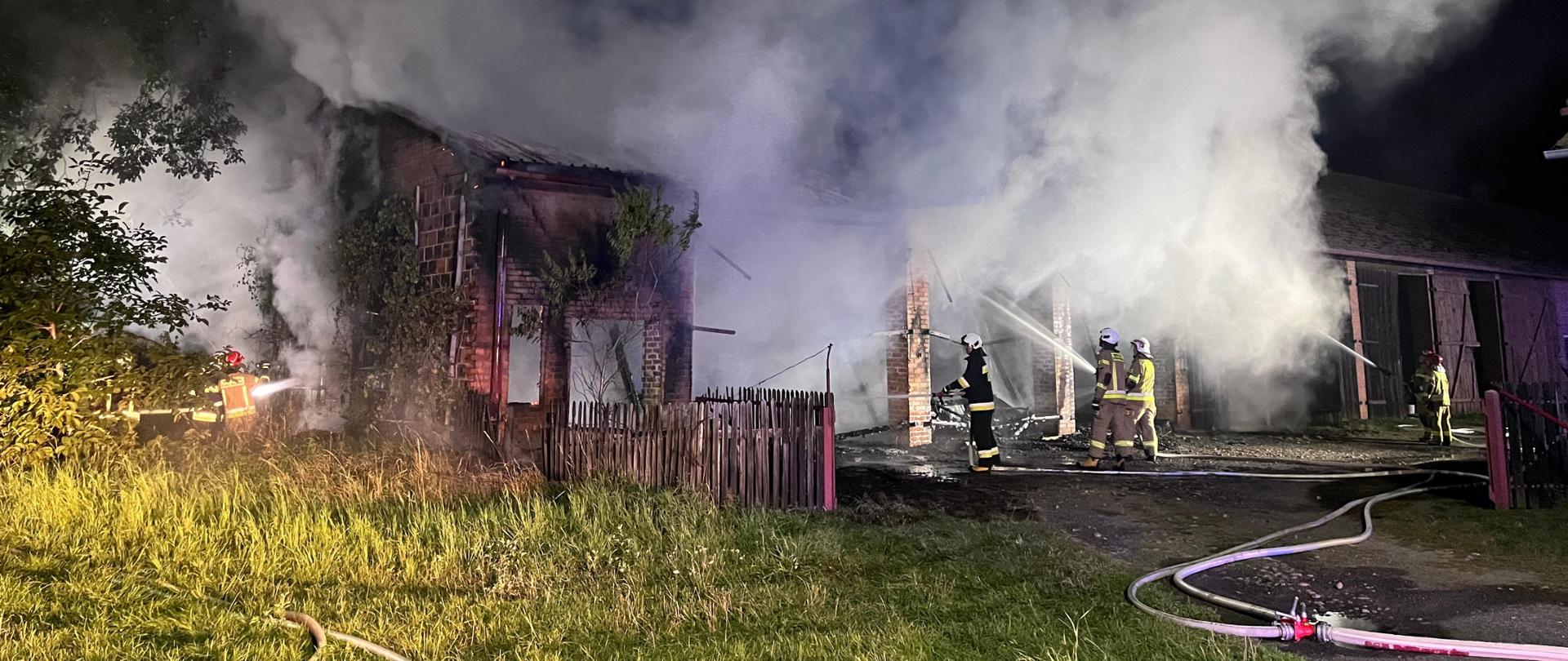 Strażacy gaszą pożar budynku. Panuje duże zadymienie. Zdjęcie wykonane w nocy.