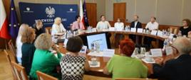 Spotkanie pożegnalne Wojewódzkiej Komisji ds. Orzekania o Zdarzeniach Medycznych. Na zdjęciu wszyscy uczestnicy spotkania siedzą przy okrągłym stole w Sali Złotej Opolskiego Urzędu Wojewódzkiego. 