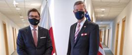 Meeting of the President of the National Atomic Energy Agency with the Chairman of the Nuclear Regulatory Commission. Dr. Łukasz Młynarkiewicz and Christopher T. Hanson are standing next to each other. In the background, the Polish and American flags.