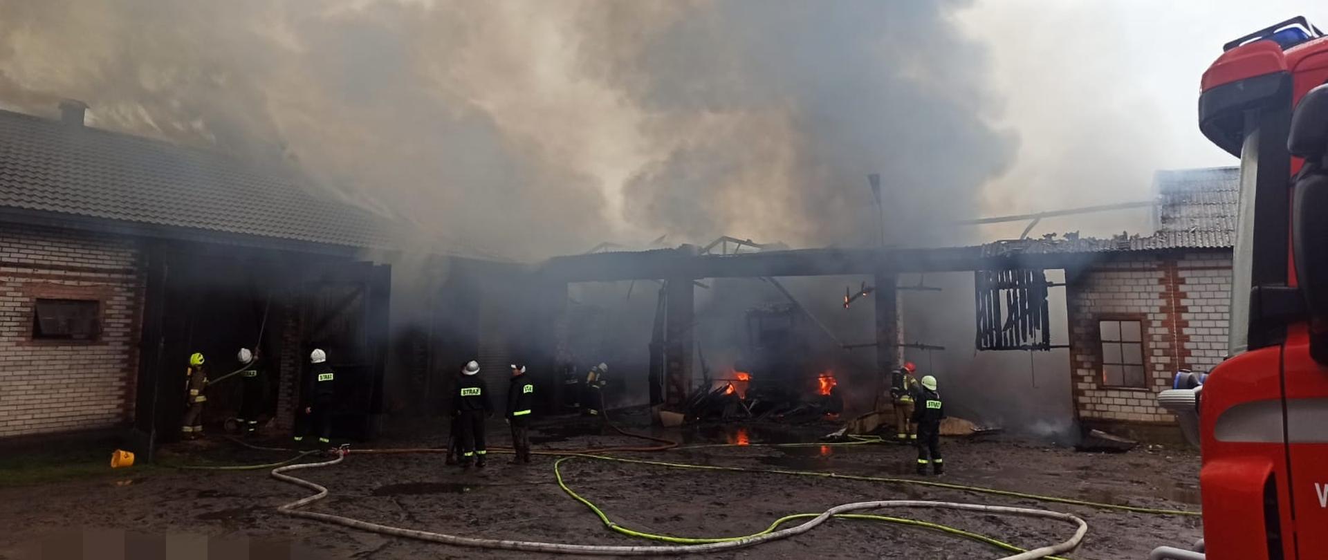 Siedmiu strażaków gasi pożar budynków gospodarczych ustawionych do siebie pod kątem prostym. Dużo dymu, dach częściowo spalony