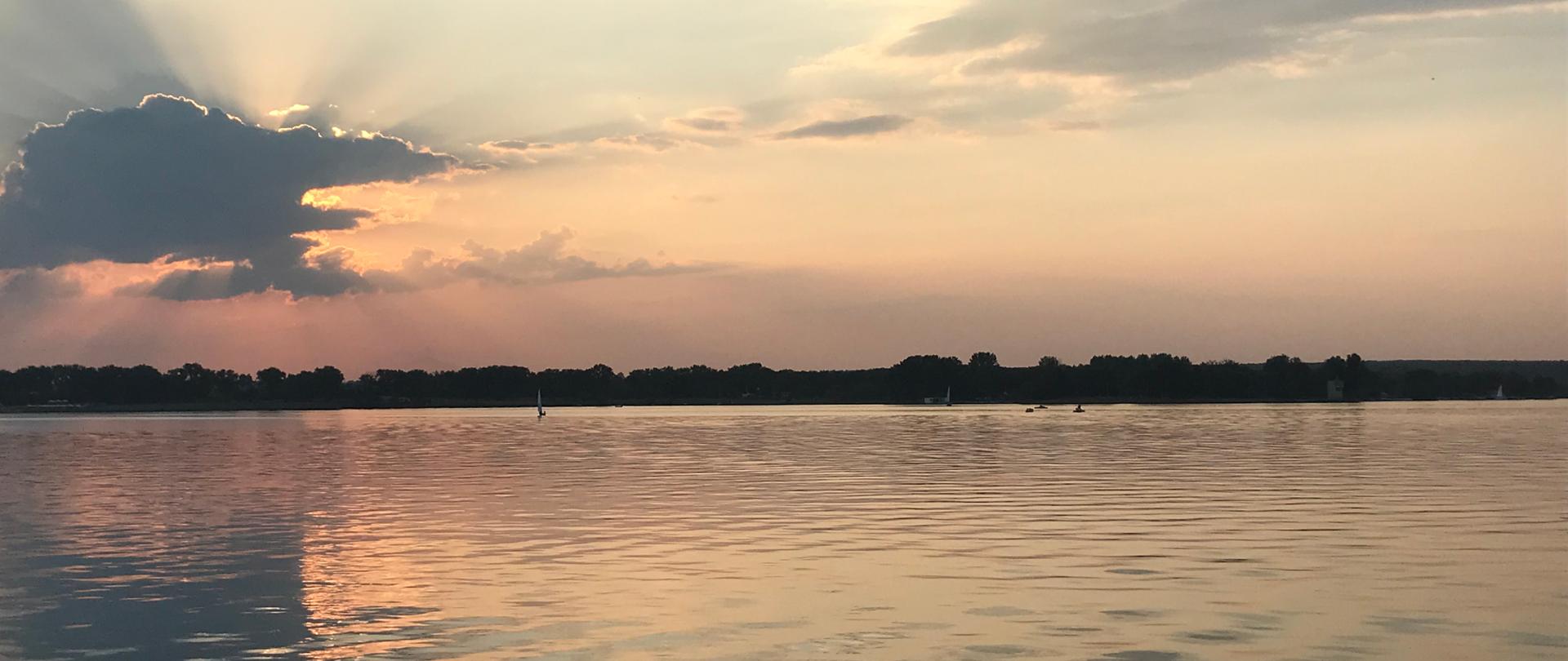 Zalew Zemborzycki przed zachodem słońca. Widoczna tafla wody, w tle drzewa. Na niebie z lewej strony ciemna chmura.