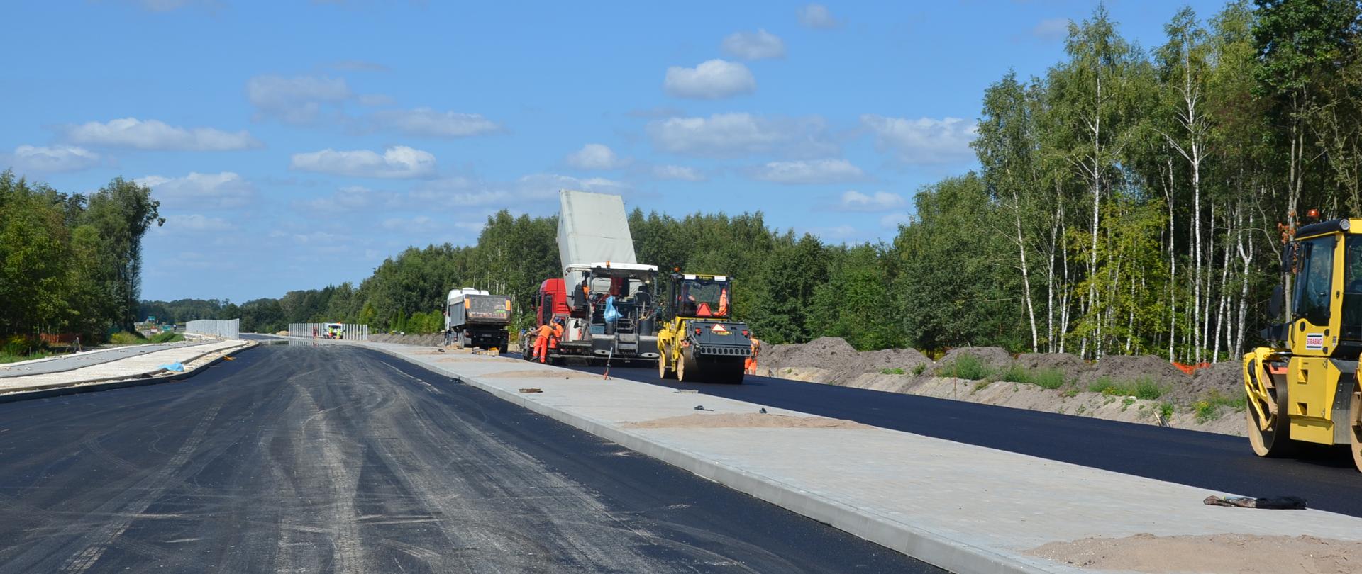 Budowa dwujezdniowej jezdni z betonowym pasem rozdziału, widoczny sprzęt.