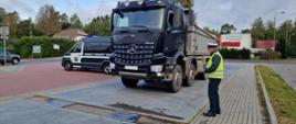 Pojazd ciężarowy podczas ważenia i stojący obok inspektor. W tle widoczny jest radiowóz Inspektoratu Transportu Drogowego.