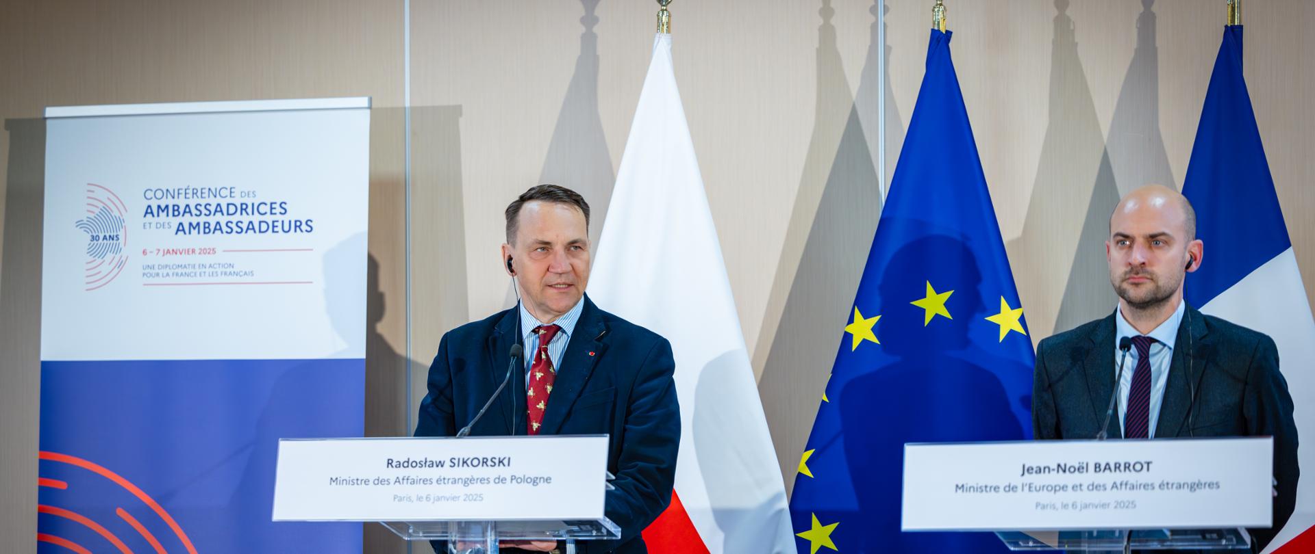 Minister Radosław Sikorski wziął udział w Naradzie Ambasadorów Republiki Francuskiej. Na zdjęciu szefowie dyplomacji Polski i Niemiec stoją na scenie, w tle flagi Polski, Unii Europejskiej i Francji.