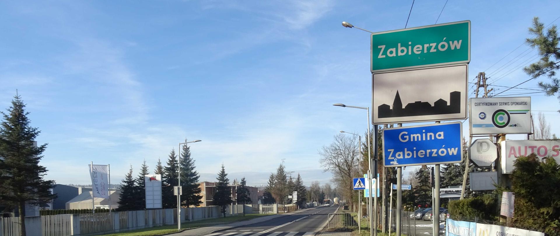 DK79 w Zabierzowie, po obu stronach chodnik i zabudowania, w oddali autobus i ciężarówka