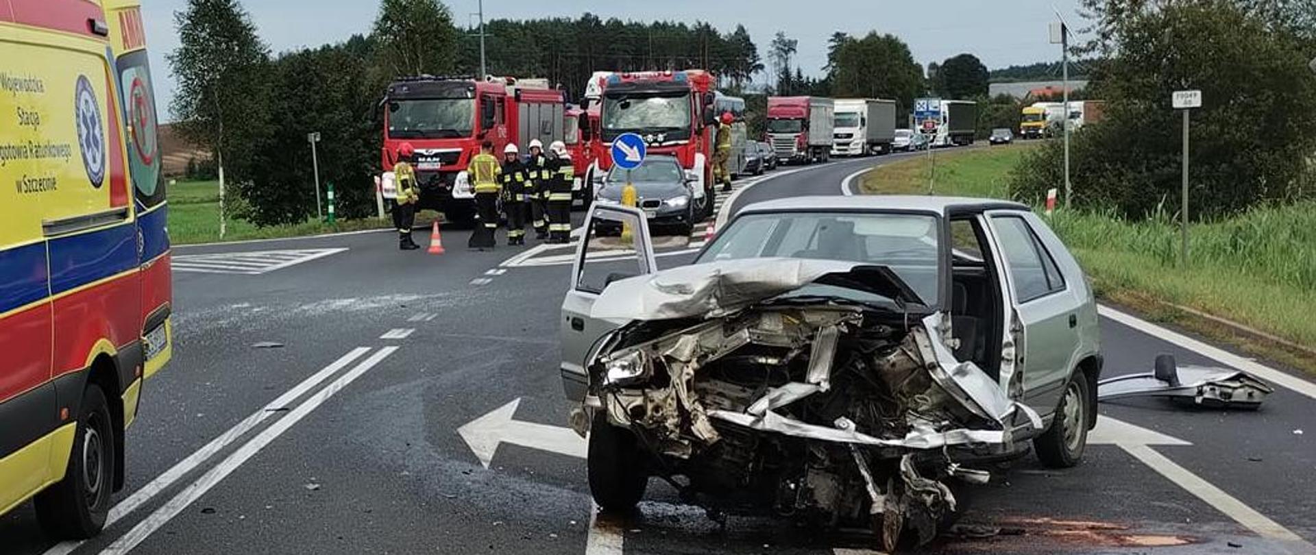 wypadek drogowy na drodze krajowej w Mirosławcu na pierwszym planie uszkodzone auto na drodze asfaltowej, w tle widoczne wozy bojowe Straży Pożarnej