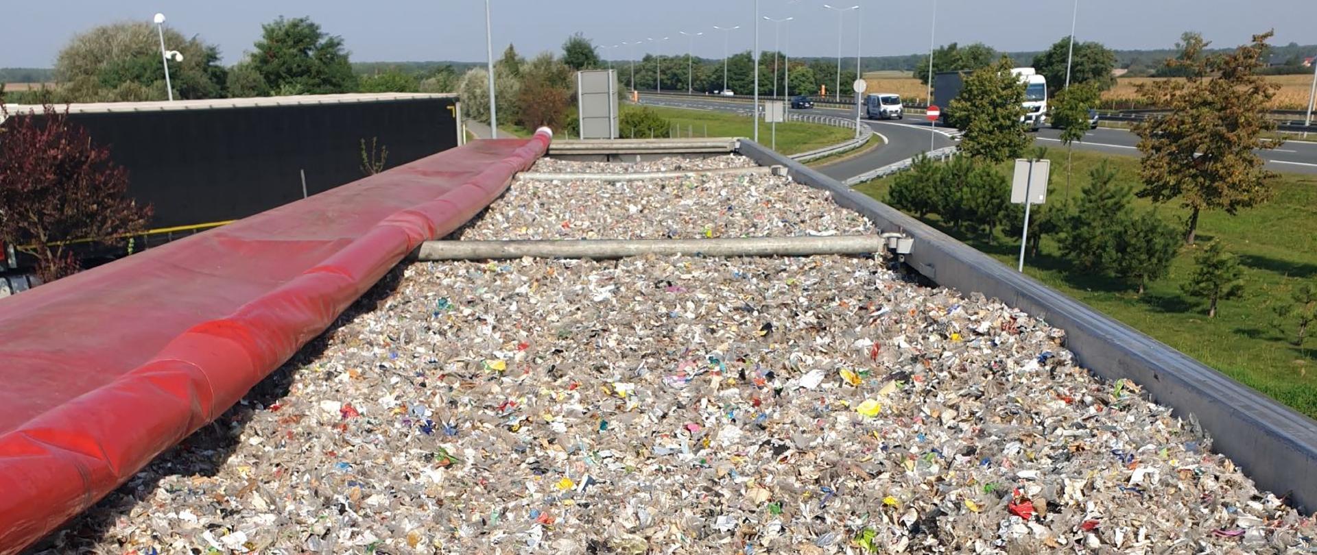 Górna część naczepy wypełniona odpadami, w tle droga.