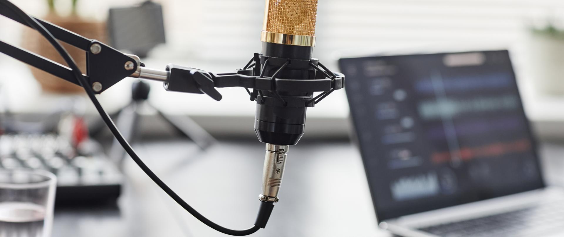 Close up of gold professional microphone in recording studio with laptop in background, copy space