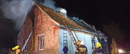 Na zdjęciu widać spalony dach budynku oraz strażaków w trakcie prowadzonych działań gaśniczych