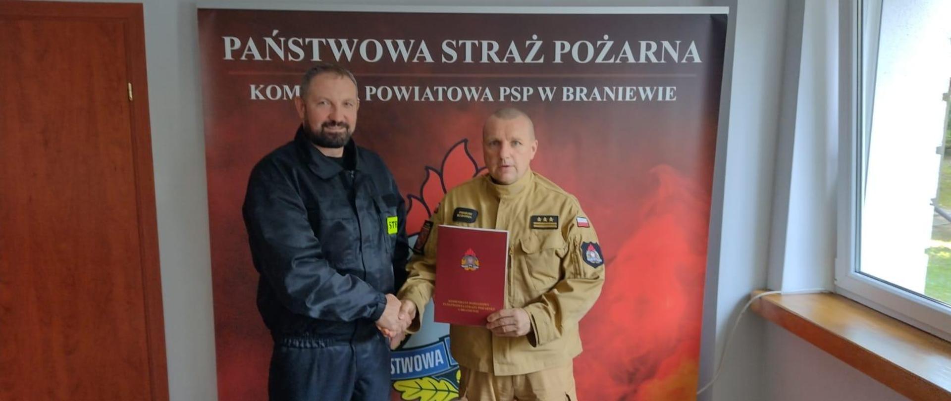 Na zdjęciu w jasnym mundurze komendant powiatowy PSP w Braniewie z lewej w czarnym mundurze prezes OSP Stare siedlisko. Stoją na czerwonym tle z napisem Państwowa Straż Pożarna.