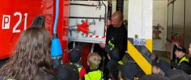 Zdjęcie przedstawia strażaka, który podczas dnia otwartych strażnic omawia dzieciom zagrożenia jakie mogą wystąpić w domach mieszkalnych oraz opowiada o pracy strażaka.