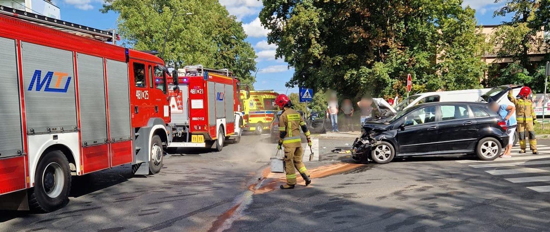 Na zdjęciu znajdują się wozy strażackie, zderzone auta oraz strażak na miejscu zdarzenia