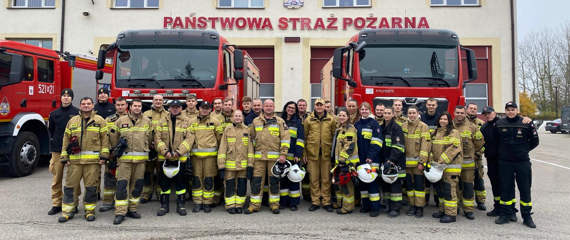 Na zdjęciu widać strażaka po zakończonym egzaminie na tle komendy oraz pojazdów.