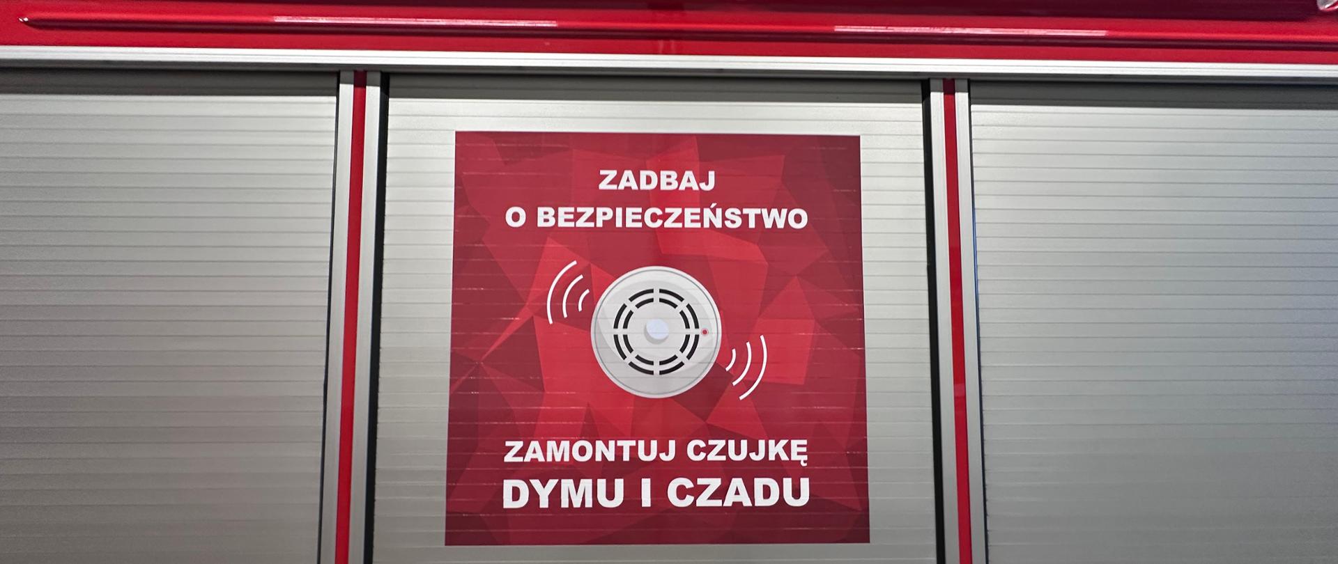 Na zdjęciu znajduje się skrytka pojazdu z plakatem dotyczącym czujki tlenku węgla i dymu