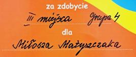 Zdjęcie przedstawia dyplom za zdobycie trzeciego miejsca. W tle graficzne wzory w kolorze niebieskim, żółtym, pomarańczowym i granatowym oraz graficznym rysunkiem instrumentów dętych.