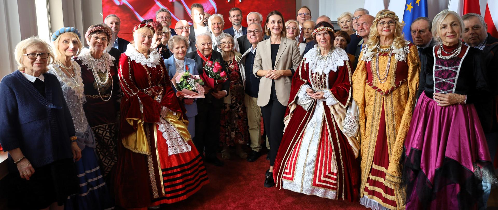 kilkanaście osób pozuje do zdjęcia, część osób jest w strojach historycznych