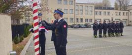 Plac KP PSP Tczew, poczet flagowy z flagą, obok ustawiony pododdział strażaków. W tle budynek komendy i ratusz.