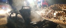 Zdjęcie przedstawia spalony wrak pojazdu wyciągniętego z palącego się budynku