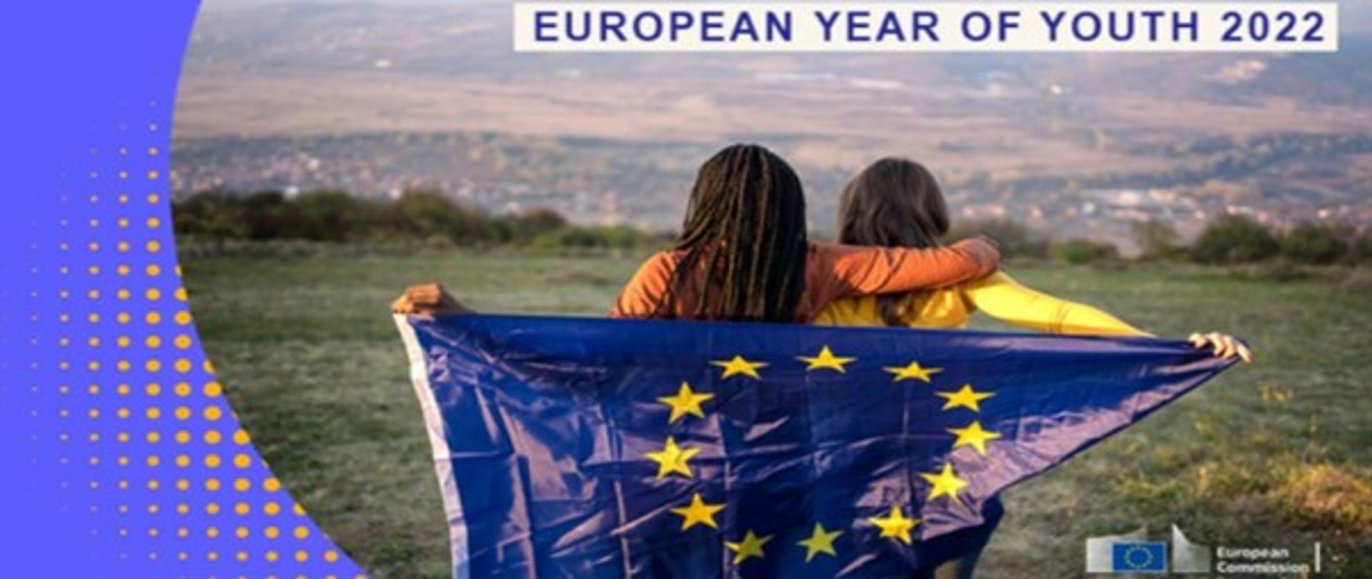Kobiety trzymające flagę Unii Europejskiej na wzgórzu. Na górze napis European Year of youth 2022