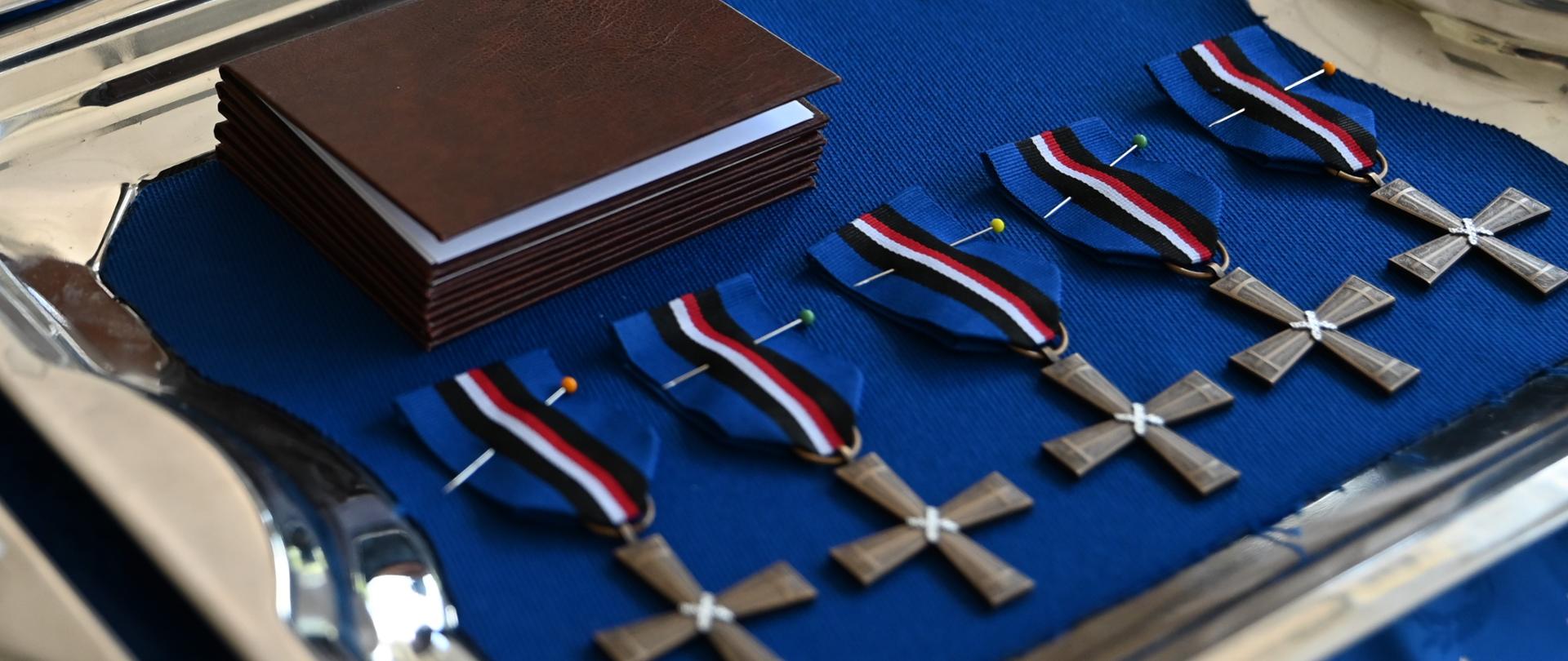 Na niebieskiej tkaninie leżą medale - odznaczenia przyznane przez Ministra Kultury i Dziedzictwa Narodowego oraz Szefa Urzędu Kombatantów i Osób Represjonowanych