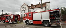 Zdjęcie przedstawia na pierwszym planie samochody pożarnicze Państwowej Straży pożarnej w Wałczu z rozwiniętą linią gaśniczą. W dalszym planie zlokalizowany jest budynek Domu Opieki Społecznej w Wałczu.