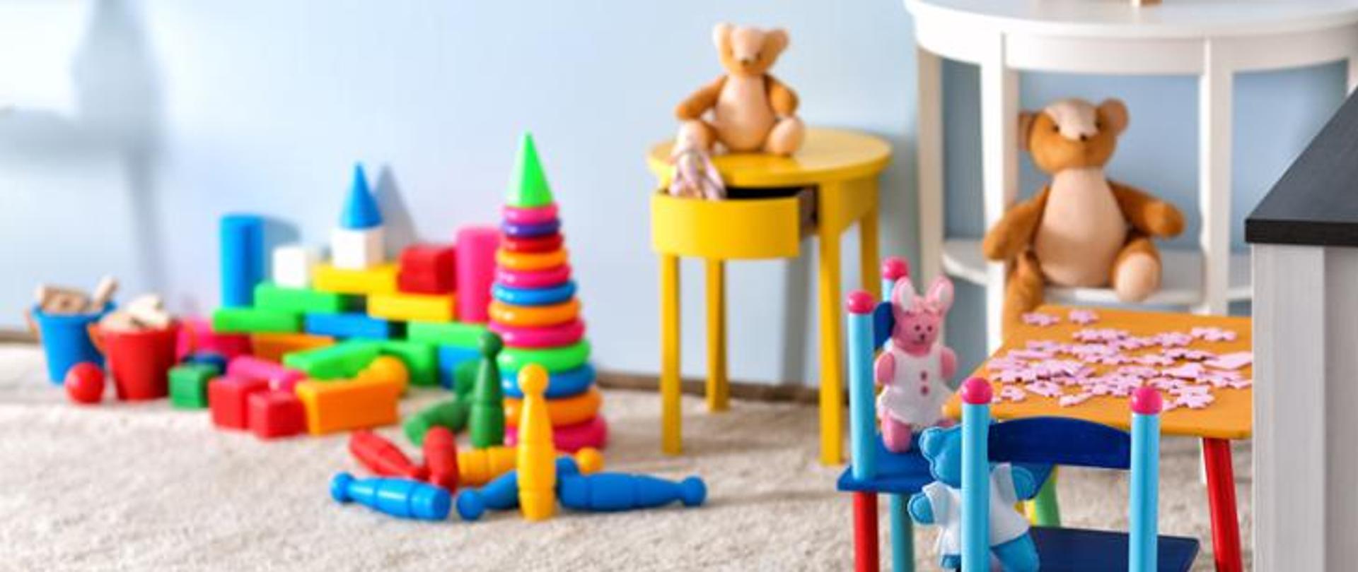 Zdjęcie przedstawia kącik zabaw dla dzieci. Widoczne są zabawki wraz ze stolikiem, na którym znajdują się puzzle. 