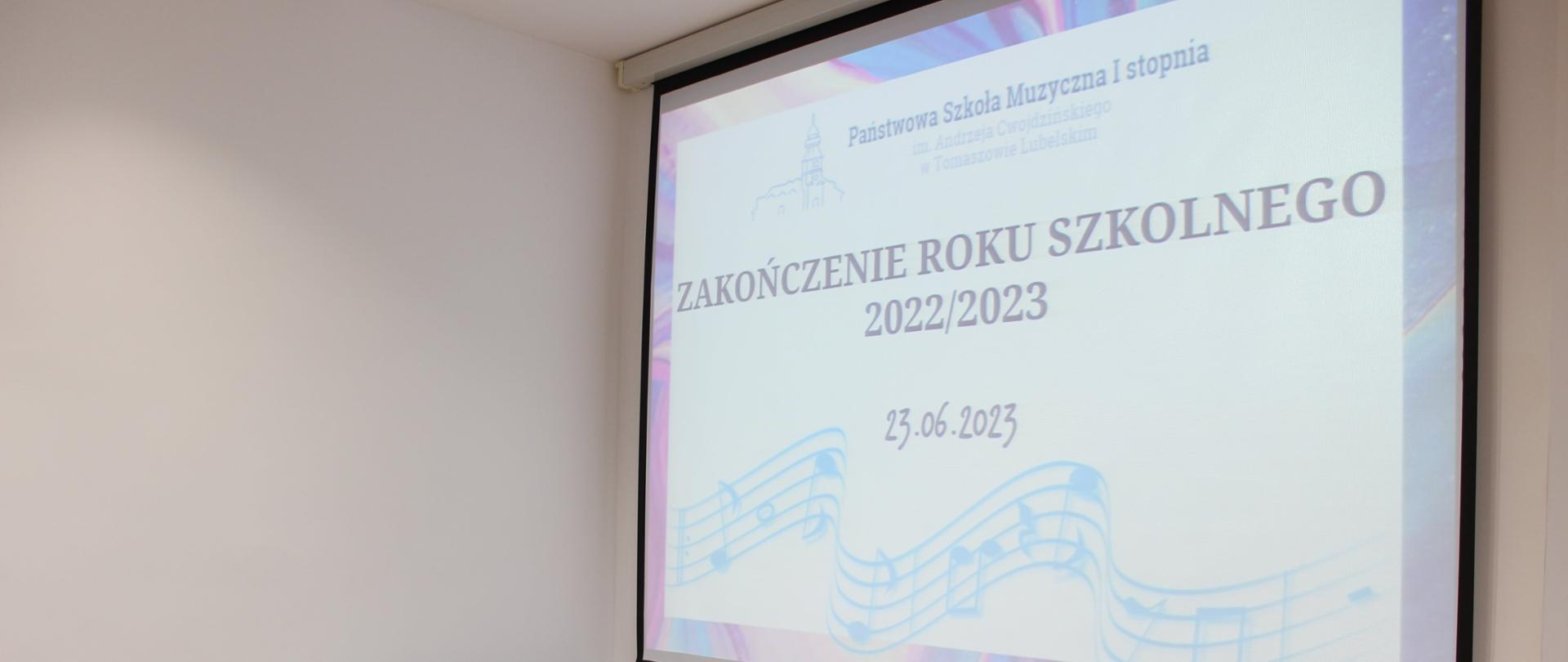 na projektorze wyświetlany napis z zakończeniem roku szkolnego 2022/2023, poniżej krzesło, stół z księgą wpisów dla uczniów oraz świadectwa