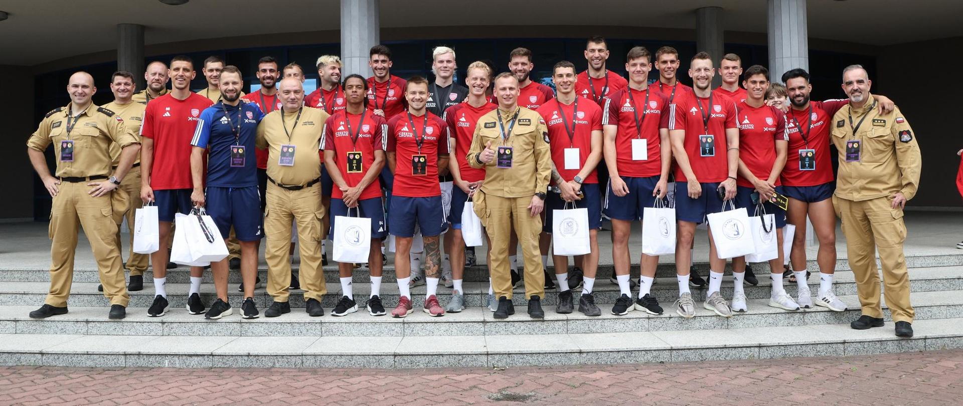 Pamiątkowe zdjęcie grupowe zawodników drużyny piłkarskiej Raków Częstochowa w towarzystwie kierownictwa oraz czterech funkcjonariuszy Centralnej Szkoły PSP