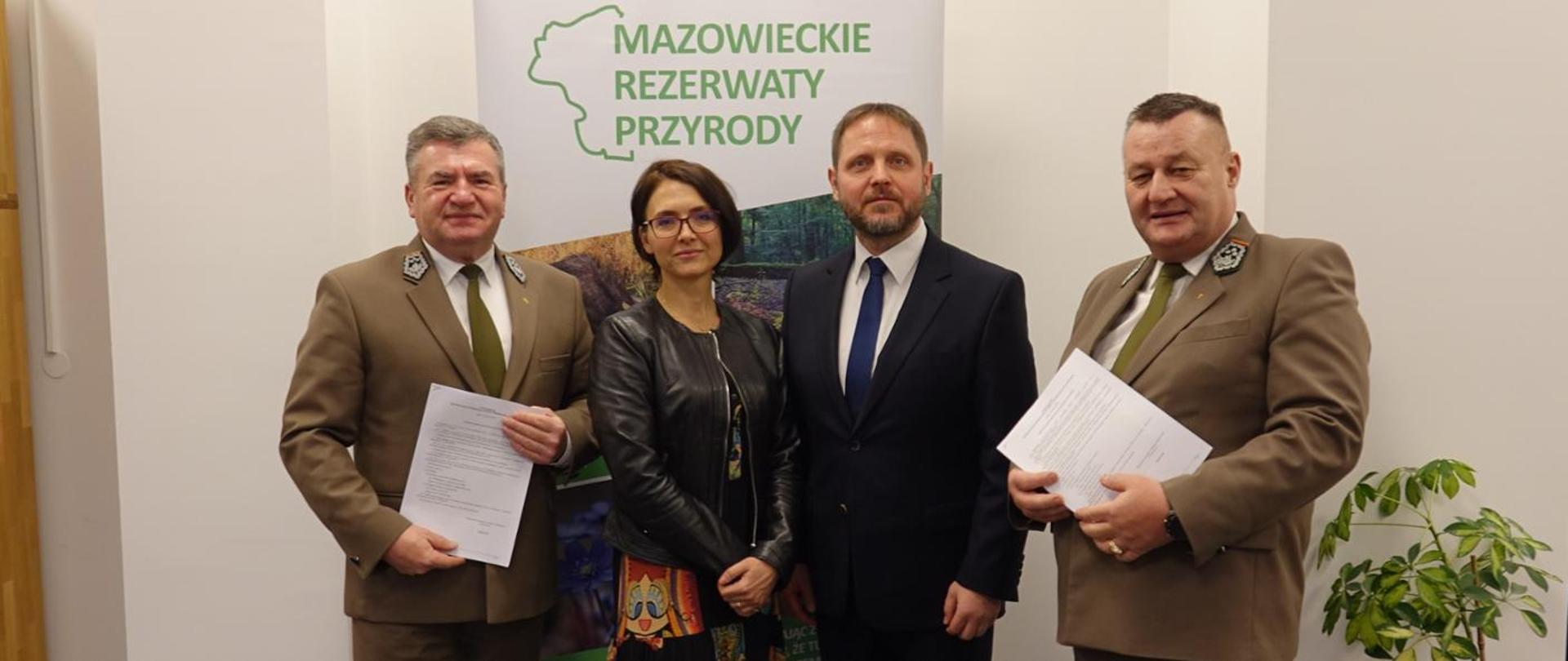 Podpisanie zarządzenia o utworzeniu rezerwatów. Regionalny Dyrektor Ochrony Środowiska w Warszawie, Jacek Lolo stoi pomiędzy trzema osobami.