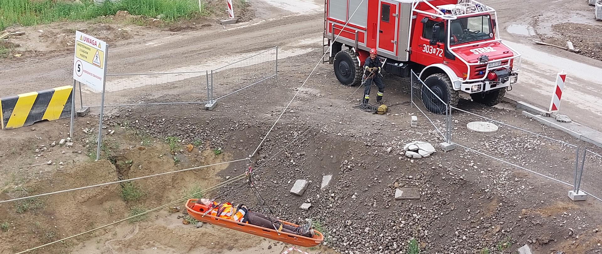 Ćwiczenia PSP, poszkodowana transportowana na placu budowy z estakady do wozu strażackiego w noszach na tzw. tyrolce