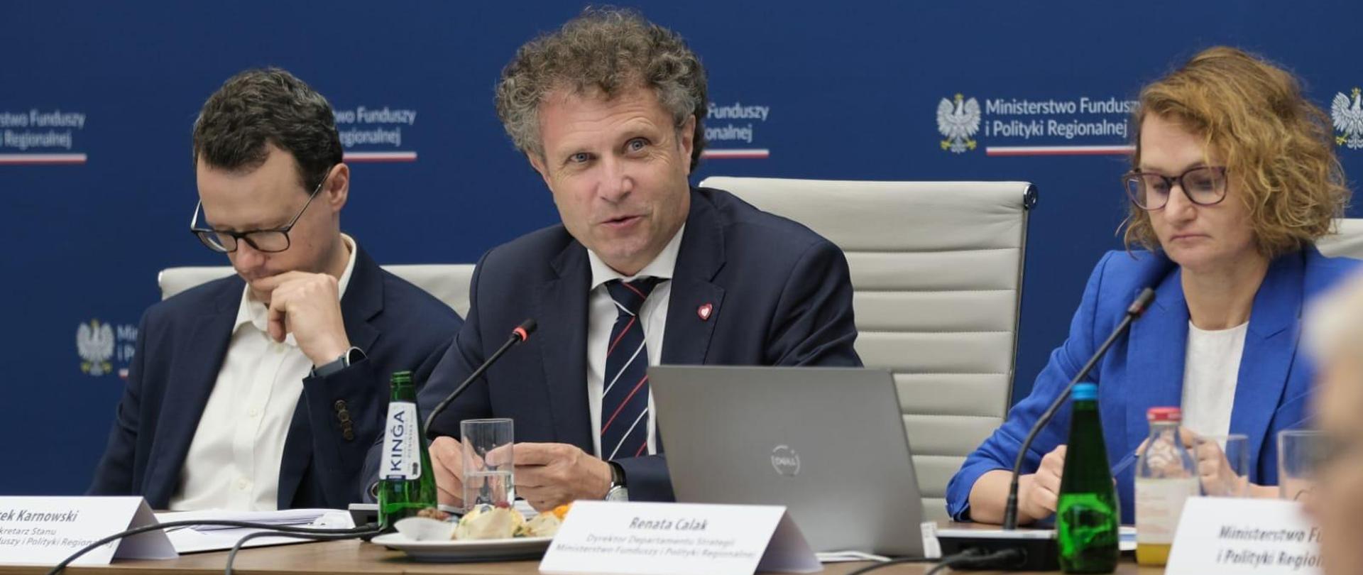 Wiceminister Jacek Karnowski siedzi przy stole w środku między dwiema innymi osobami.