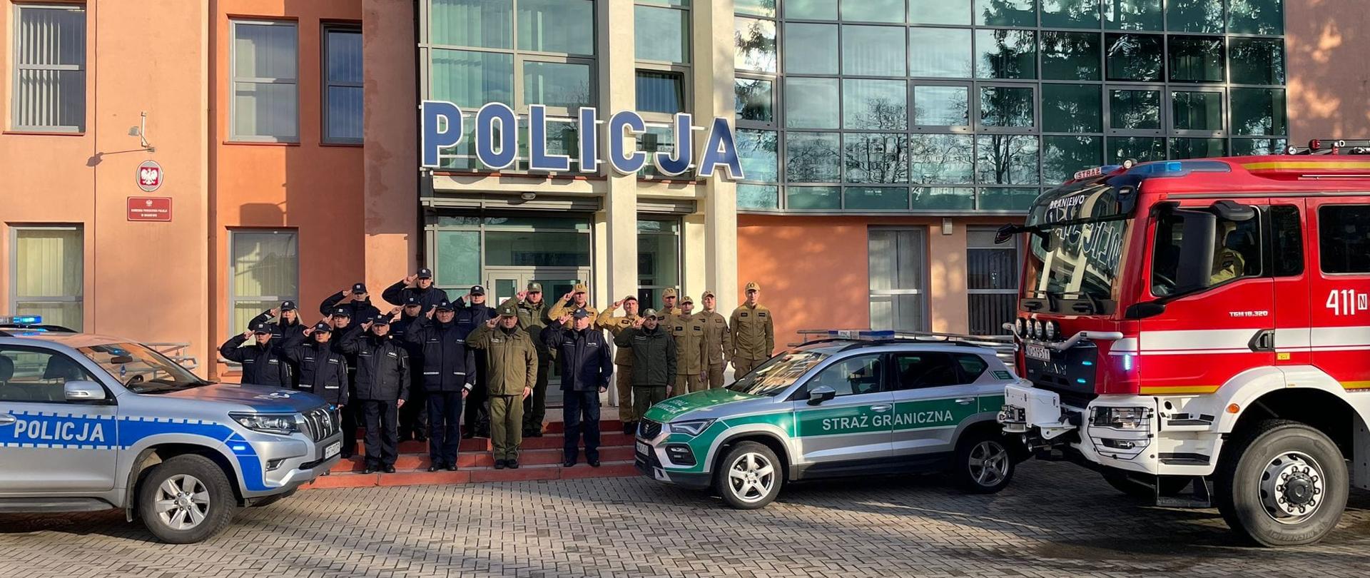 Oddali hołd zastrzelonemu policjantowi. Na tle komendy Policji w Braniewie stoją funkcjonariusze Policji, Straży Granicznej oraz Strażacy PSP.