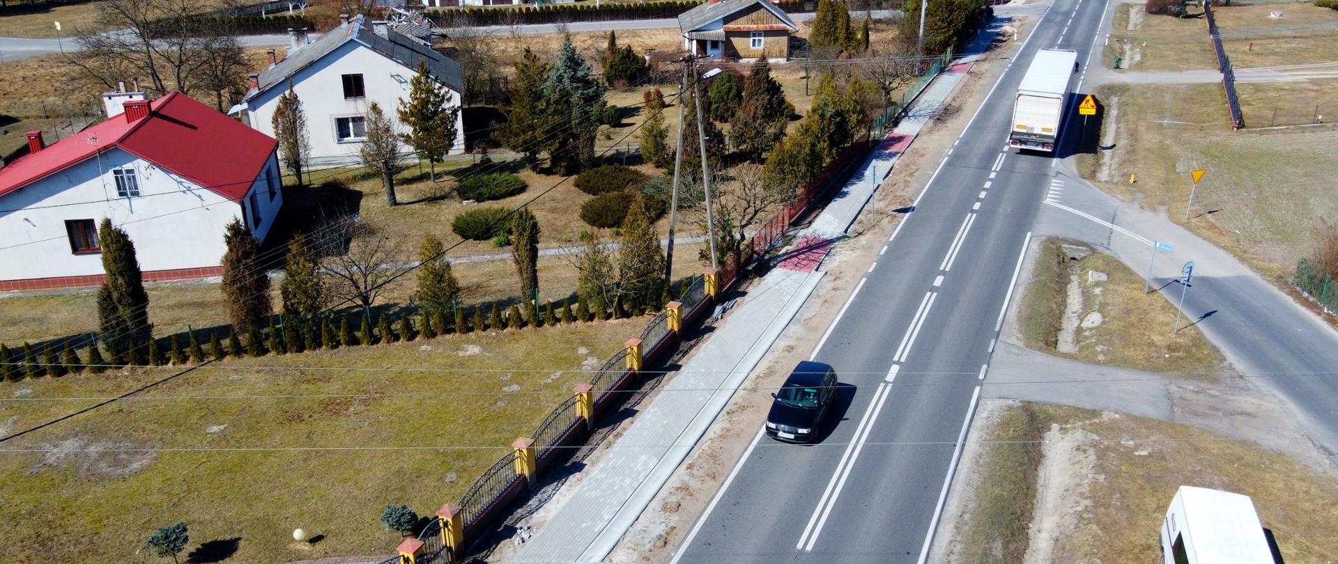 Zdjęcie z drona, świeci słońce, widać chodnik, drogę i samochody.