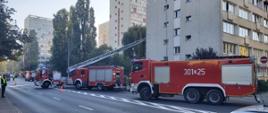 Na jezdni 3 wozy strażackie: średni, ciężki i rozstawiona drabina mechaniczna z JRG 1 w tle wieżowce przy ulicy Malczewskiego