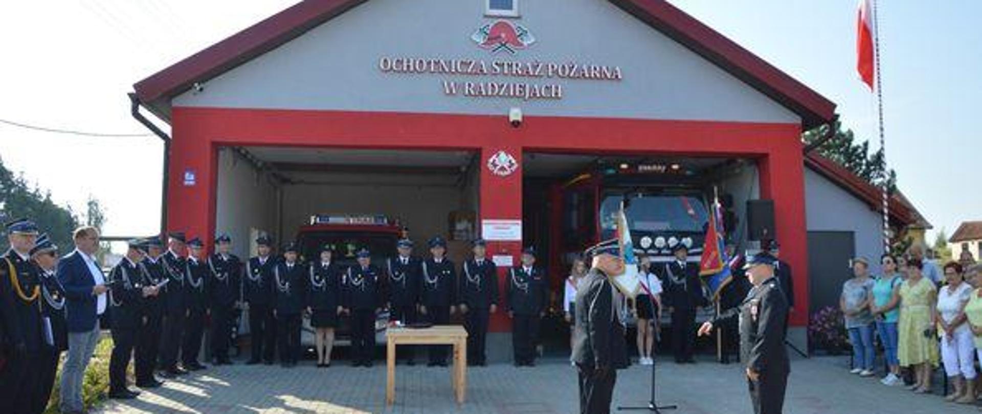 Uroczyste otwarcie rozbudowanej remizy OSP w Radziejach strażacy i goście stoją na zbiórce przed strażnicą. 