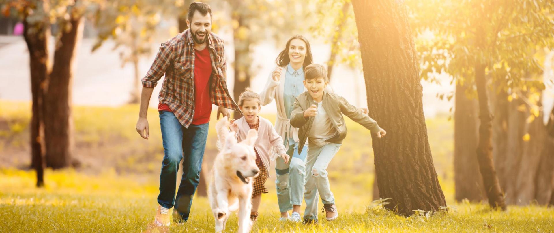 Na zdjęciu jest biegnąca rodzina wraz z psem w parku.