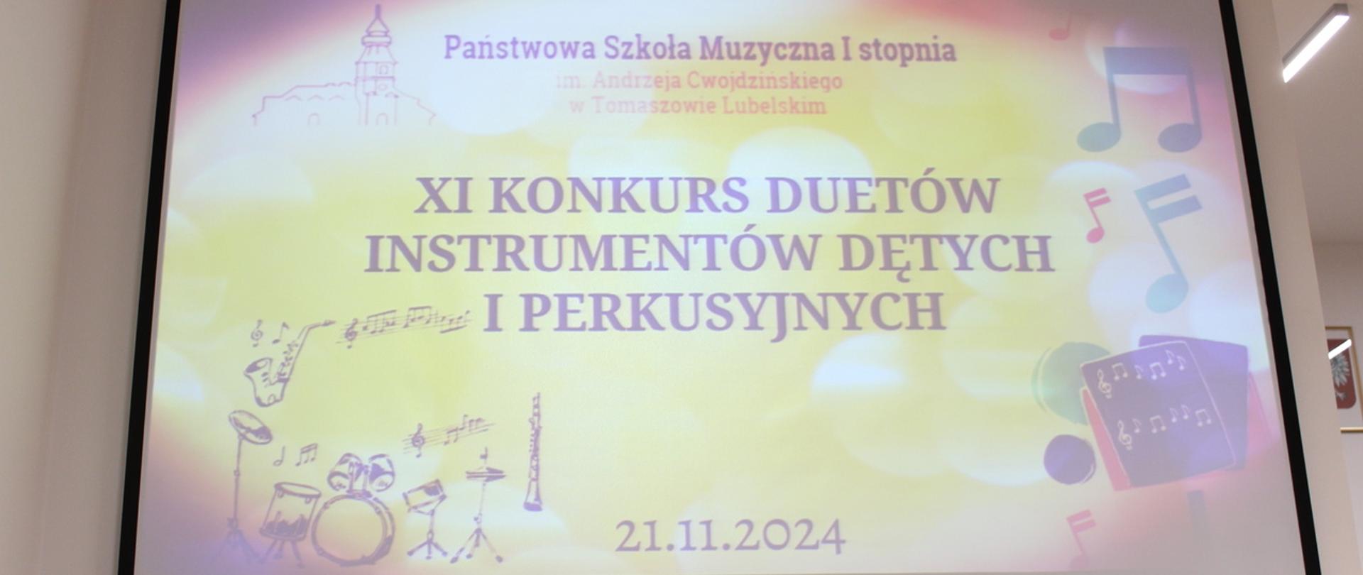 wyświetlony plakat na projektorze, przedstawia w części głównej tytuł XI Konkurs Duetów Instrumentów Dętych i Perkusyjnych, jest kolorowy, zawiera ilustracje, po lewej stronie instrumenty dęte saksofon, klarnet, zestaw perkusyjny oraz po prawej stronie nuty, pulpit z nutami