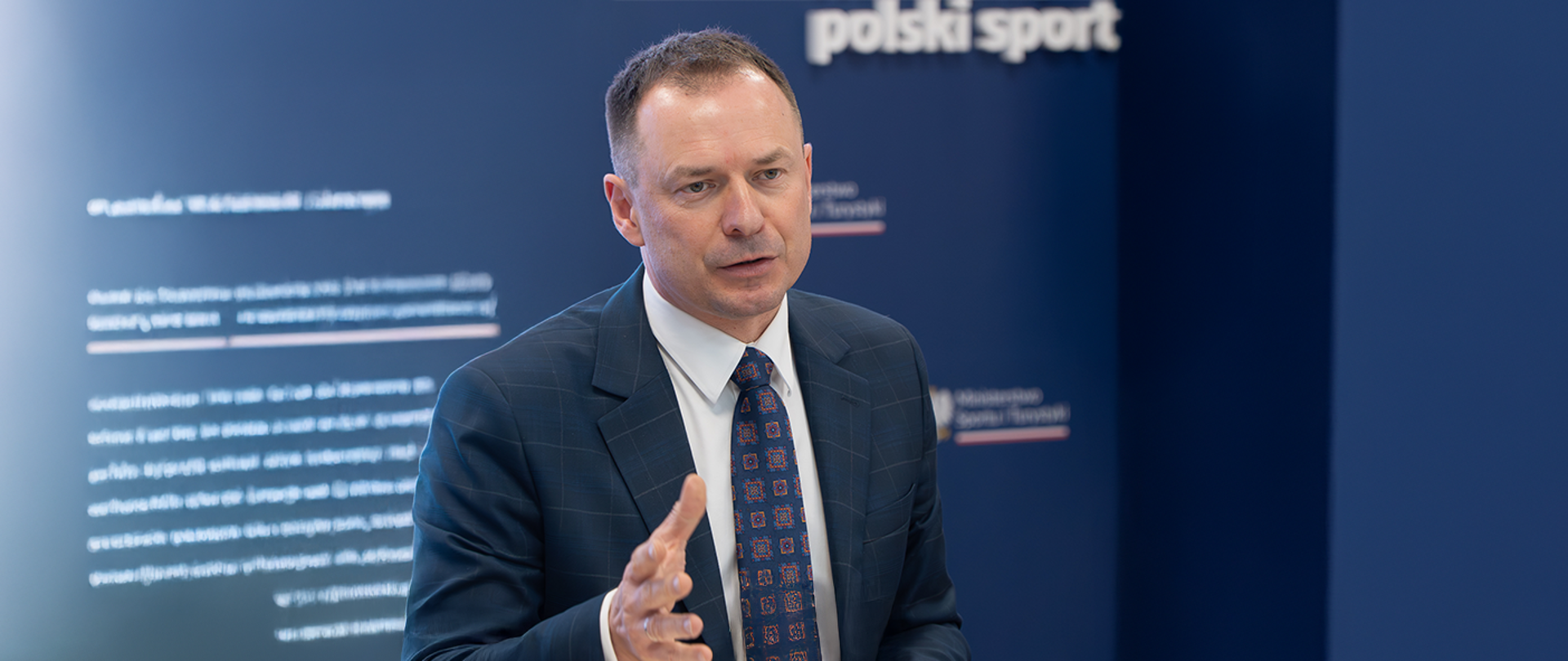 Minister Piotr Borys podczas spotkania z branżą turystyczną na tle ścianki z logiem ministerstwa