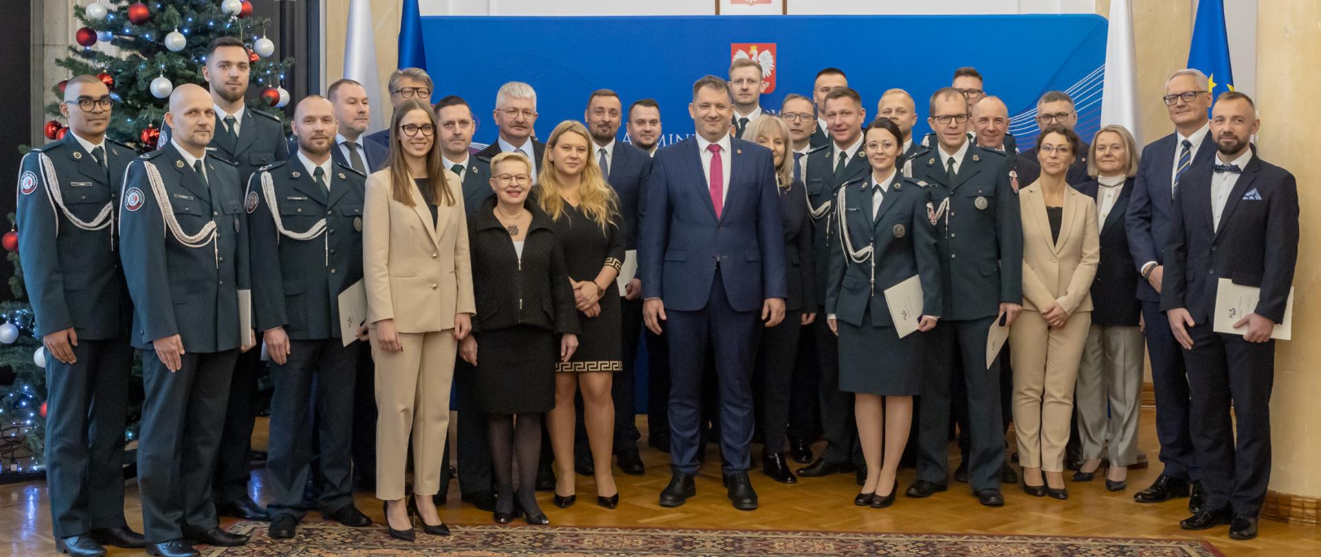 Minister Marcin Łoboda, Minister Małgorzata Krok, pracownicy i funkcjonariusze KAS na tle ścianki z Godłem Polski.