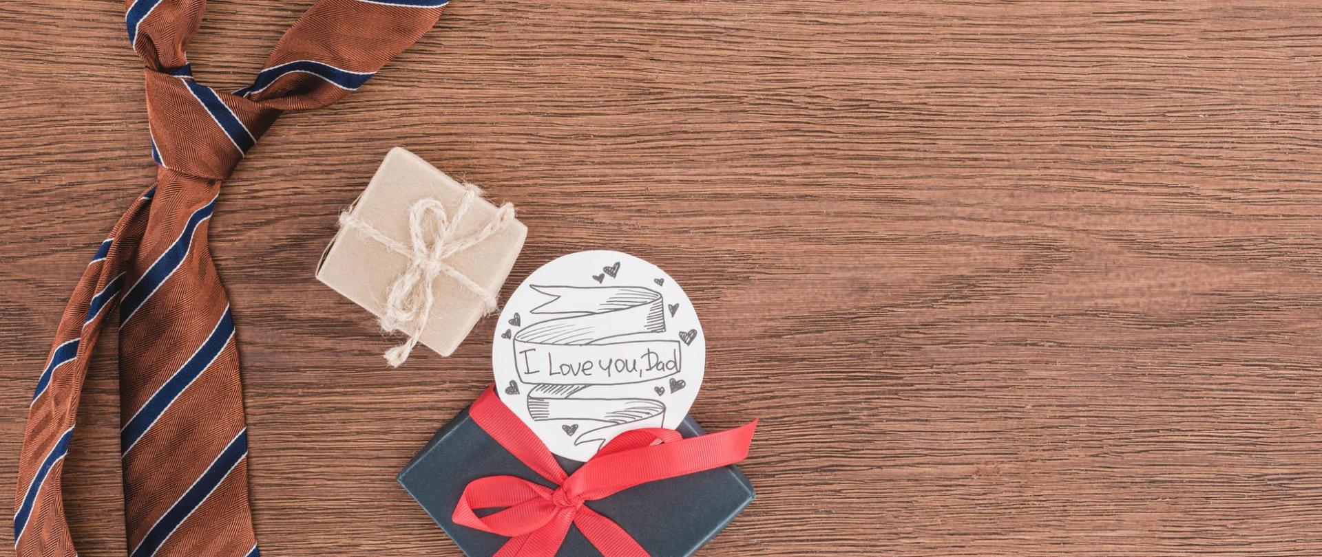 Na zdjęciu na drewnianym blacie jest krawat, dwa pudełka prezentowe oraz okrągła plakietka z napisem "I love you Dad".