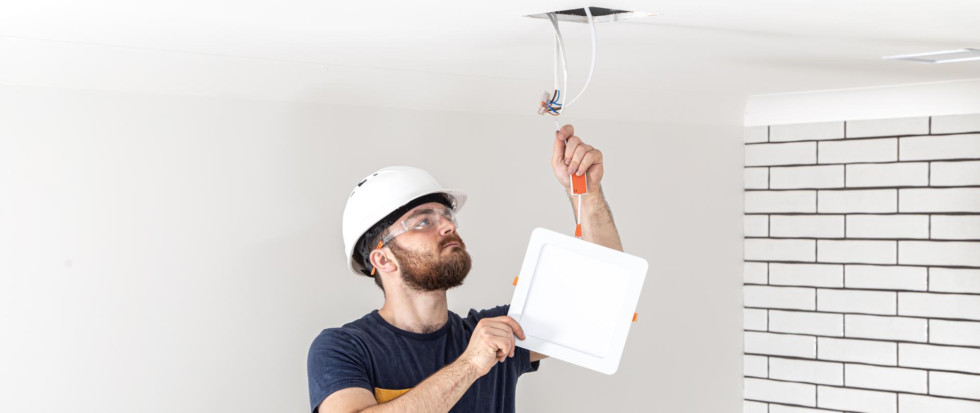 Electrician Builder at work, installation of lamps at height. Professional in overalls with an electrical tool. On the background of the repair site. The concept of working as a professional.