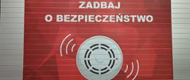 Na zdjęciu widnieje naklejka umieszczona na boku pojazdu pożarniczego o treści " Zadbaj o swoje bezpieczeństwo - zamontuje czujkę dymu i czadu"
W centralnym miejscu naklejki zamieszczono czujkę.