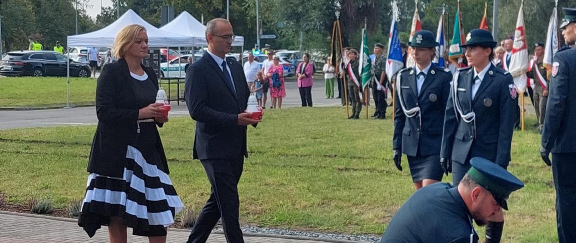 kobieta i mężczyzna stoją pod pomnikiem Polskich Celników w Malborku, w dłoniach trzymają znicze