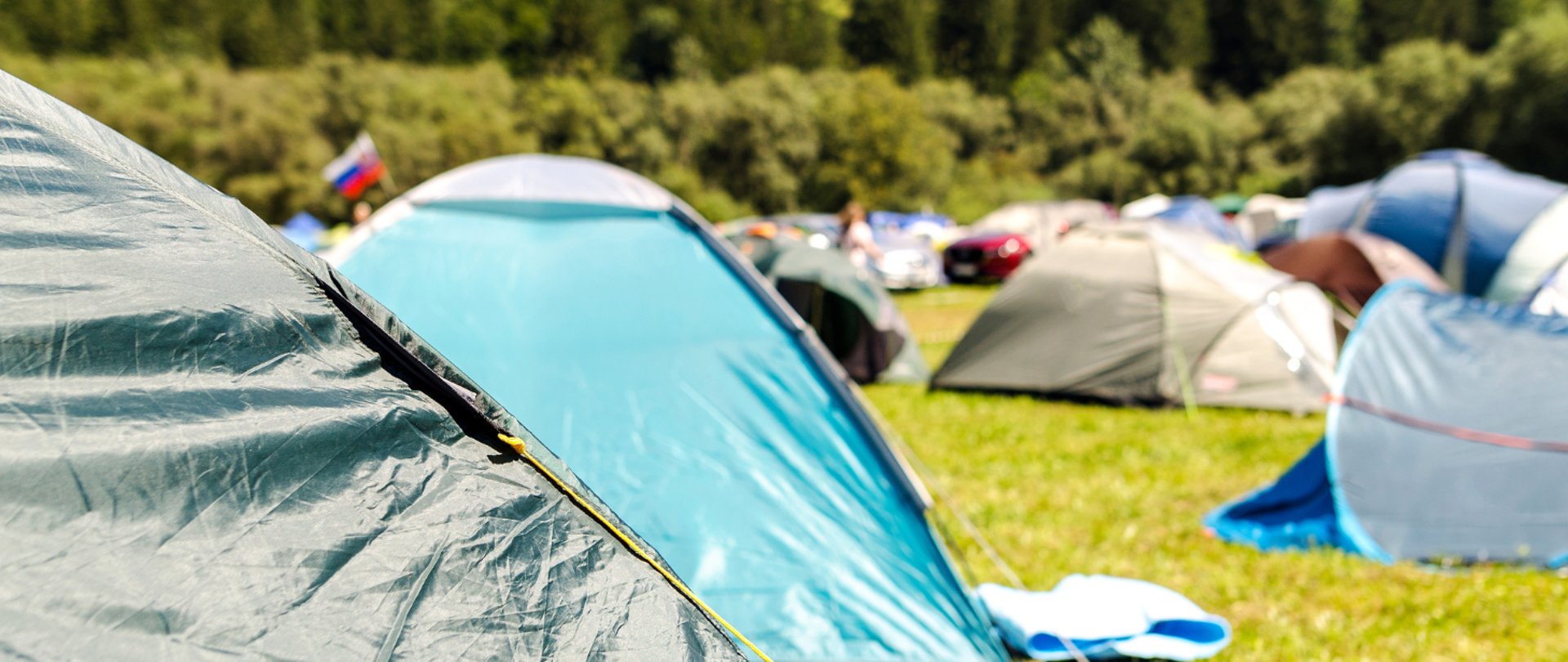 Na zdjęciu znajduje się pole namiotowe na którym rozstawione są różnokolorowe namioty. Na pierwszym planie z lewej strony znajduje się namiot w kolorze ciemnej zieleni.