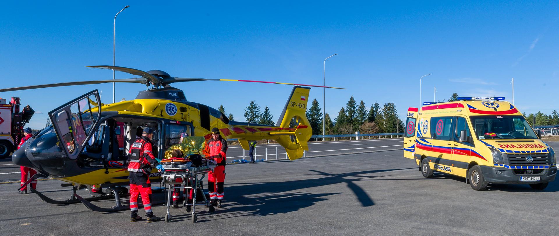 Ćwiczenia służb ratowniczych na drodze ekspresowej S7. Ratownicy medyczni transportują z karetki do śmigłowca osobę poszkodowaną w zdarzeniu drogowym.