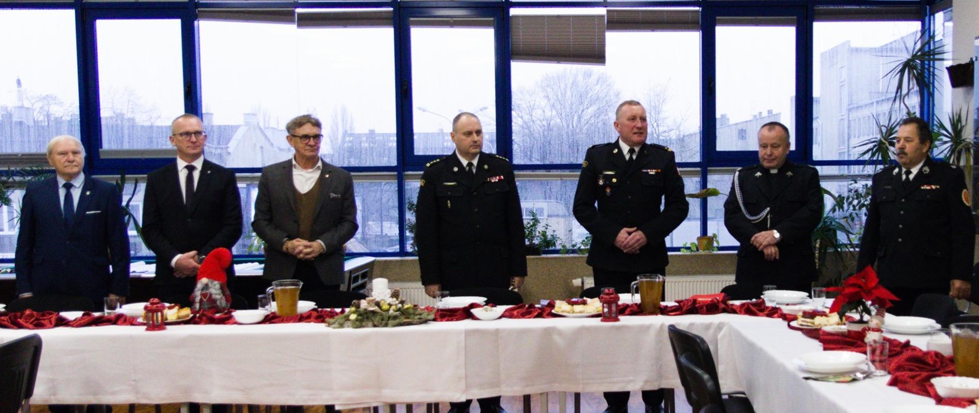 Zdjęcie wykonane podczas części oficjalnej spotkania wigilijnego w KP PSP w Pabianicach. Od lewej stoją: Jerzy Rzepkowski, Arkadiusz Jaksa, Krzysztof Habura, st. bryg. Piotr Rudecki, mł. bryg. Jacek Karcz, ks. Jerzy Rzepkowski oraz dh Roman Figiel.