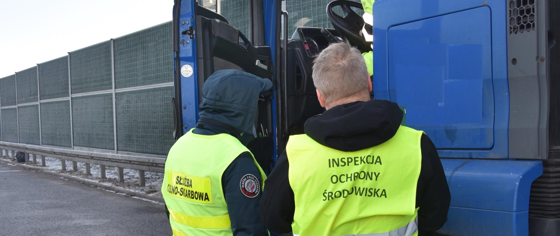 Inspektor Wojewódzkiego Inspektoratu Ochrony Środowiska w Warszawie wraz z funkcjonariuszem Krajowej Administracji Skarbowej kontroluje samochód ciężarowy.