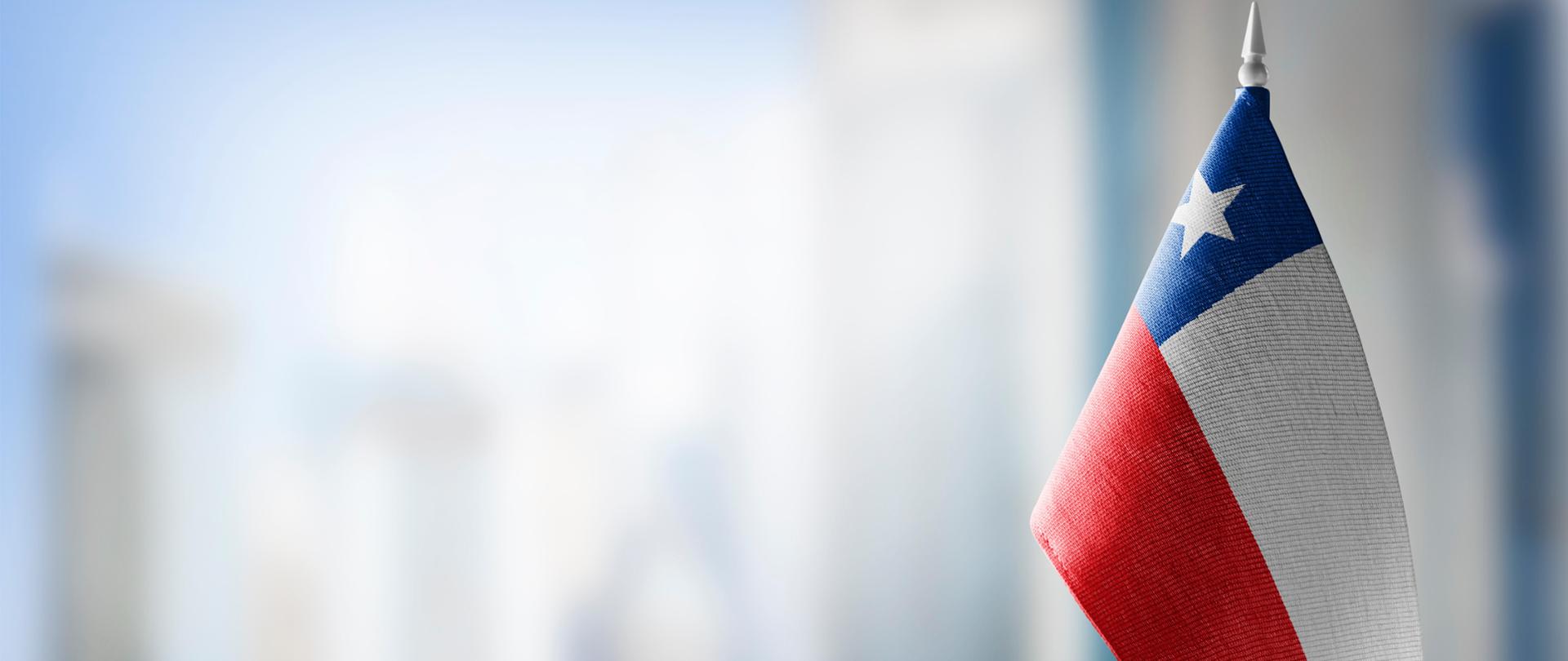 A small flag of Chile on the background of an urban abstract blurred background.